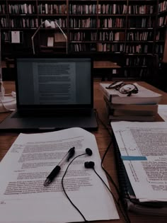 a laptop computer sitting on top of a wooden desk next to books and headphones