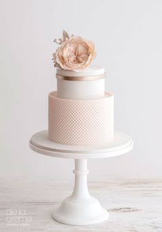 a three tiered white cake with a flower on the top and bottom, sitting on a pedestal