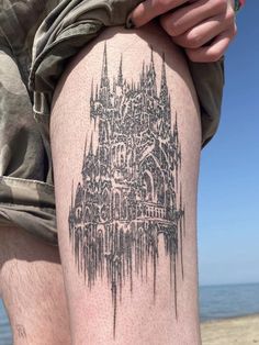 a person with a tattoo on their leg near the water and a castle in the background