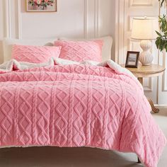 a bed with pink comforter and pillows in a room next to a lamp on a table