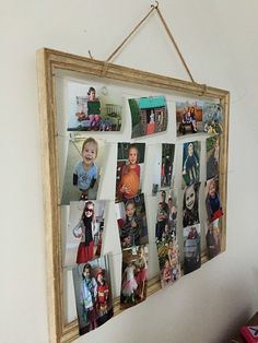 a wooden frame hanging on the wall with many pictures attached to it and a string