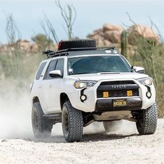 a white four - doored toyota truck driving down a dirt road in the desert