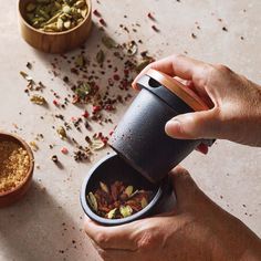 a person holding a cup with spices in it next to two bowls filled with dried herbs