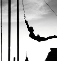 a person hanging upside down on a rope in the air with buildings in the background