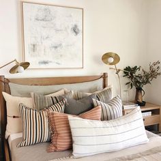 a bed topped with lots of pillows next to a lamp and painting on the wall