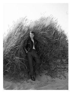 a man sitting on top of a pile of grass next to tall dry grass covered ground