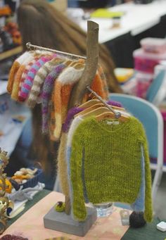 sweaters are hanging on a rack in a room with other items and people sitting at tables