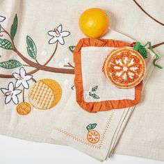 an orange sitting on top of a table next to a piece of cloth with embroidered designs