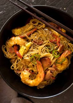 a black bowl filled with noodles and shrimp next to chopsticks on a table