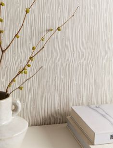 a white vase with some flowers in it next to a stack of books on a table