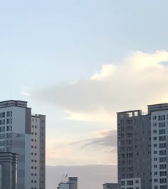 some very tall buildings in the distance with a plane flying over them on a cloudy day