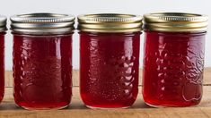 four jars filled with red liquid sitting on top of a wooden table