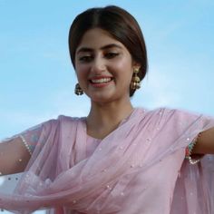 a woman in a pink sari smiles at the camera with her hands on her hips