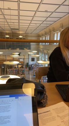 a woman sitting at a table with a laptop computer in front of her and papers on the desk