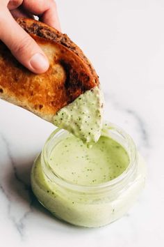 a person dipping something into a small jar filled with green sauce on top of a table