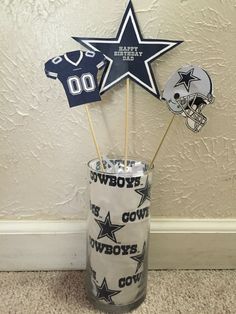 a glass vase filled with cupcake toppers and two cowboys pinwheels in front of a wall