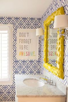 a bathroom with blue and white wallpaper has a sink, mirror, and window