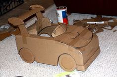 a cardboard car sitting on the floor next to a can of paint and some scissors