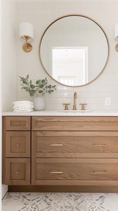 a bathroom vanity with a round mirror above it and gold faucets on the side