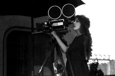 black and white photograph of a woman with an umbrella looking at a movie projector