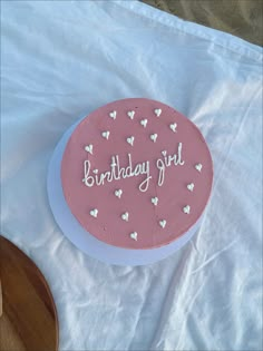 a pink birthday cake sitting on top of a white table cloth covered in frosting