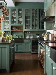 a kitchen with green cabinets and wooden floors, pots and pans hanging from the ceiling