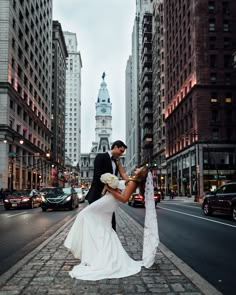 a bride and groom kissing in the middle of a city street with tall buildings behind them