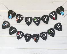 black guitar picks with happy birthday written on them are hanging from a string against a white wooden background