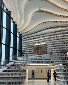 two people are standing in the middle of a large room with many bookshelves