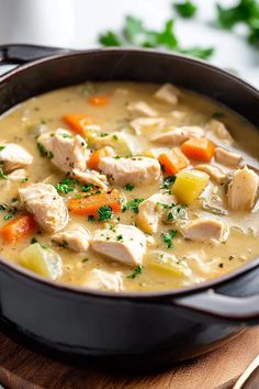 a pot filled with chicken and vegetables on top of a wooden cutting board