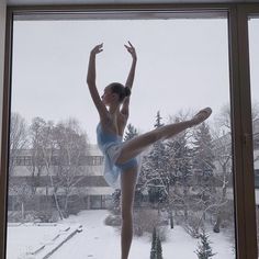 a ballerina standing in front of a window with snow on the ground and trees outside