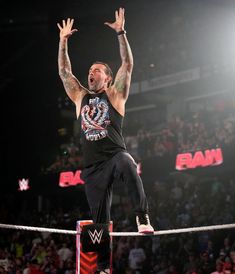 a man standing on top of a rope with his hands up in the air while holding a wrestling ring