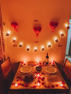 the table is set for two with plates and candles on it, surrounded by red rose petals