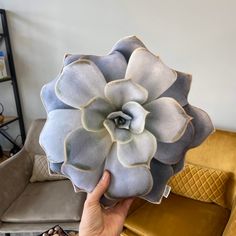 a person holding up a large flower in front of a yellow couch with other furniture