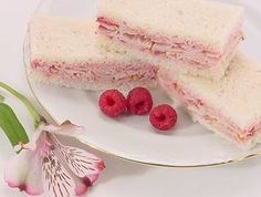 two sandwiches on a plate with raspberries next to it and a pink flower