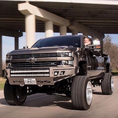 a black truck driving down a street under a bridge