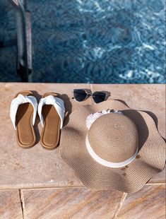 a hat, sunglasses and flip flops sit on the edge of a pool