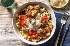 a white bowl filled with pasta and meatballs on top of a blue napkin next to silverware