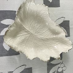 a white leaf shaped dish sitting on top of a tablecloth covered table with black and white designs