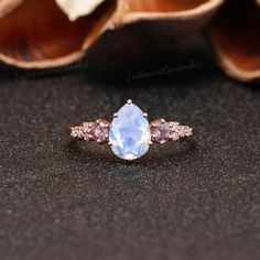 an oval shaped blue topazte and pink diamond ring on a black surface with flowers in the background