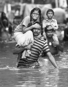 black and white photograph of people in water with one child on his shoulders, while the other is carrying an adult