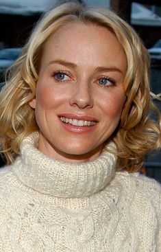 a woman with blonde hair wearing a white turtle neck sweater and smiling at the camera