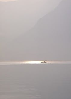 a lone boat in the middle of an empty body of water with mountains in the background