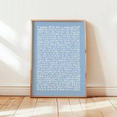 a blue framed print with white writing on it in front of a wooden floor and wall