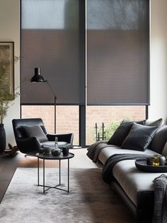 a living room with two couches and a table in front of large windows that have shades on them