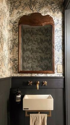 a white sink sitting under a mirror in a bathroom next to a wooden framed mirror