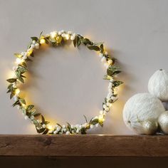 a wreath made out of white balls and greenery on top of a wooden shelf