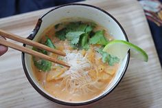 a person holding chopsticks over a bowl of soup with noodles and vegetables in it