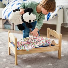 a young child playing with a stuffed panda bear in a wooden toddler's bed