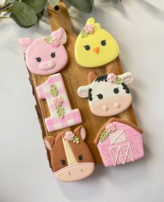 decorated cookies with farm animals on a wooden board next to a potted plant and green leaves